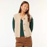 Chaleco de punto beige con textura de ochos, sin mangas, con cuello redondo y cierre frontal con botones grandes dorados.