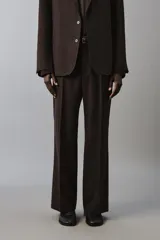 Pantalón de traje flare fit para hombre, confeccionado en tejido con lana, en color marrón oscuro. Presenta tiro medio, trabillas para cinturón, cierre frontal con cremallera y botón, bolsillos laterales y raya central marcada en las perneras.