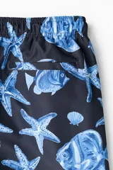 Short de baño azul marino con estampado de peces, estrellas de mar y caracolas en tonos azules y blancos. Cuenta con cintura elástica con cordón de ajuste.