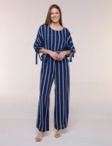 Enterito largo de crepe color azul marino con diseño de rayas verticales blancas. Cuenta con escote redondo, mangas tres cuartos con detalles de lazos en los puños, cintura elastizada con lazo extraíble para ajustar, bolsillos laterales y pantalón de corte amplio.