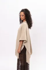 Ruana de tejido de punto en color arena, con diseño cruzado, escote en V y terminaciones con flecos en el ruedo. Incluye un parche de cuero con la marca Pura Lana en la parte frontal.