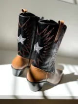 Bota tejana de cuero color marrón claro con puntera fina, caña media con bordados en negro y blanco, y taco bajo.