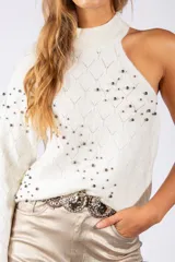 Sweater de punto negro con diseño asimétrico de un solo hombro y cuello alto. Presenta un patrón de rombos en relieve y está decorado con pequeñas tachas metálicas distribuidas por toda la prenda.