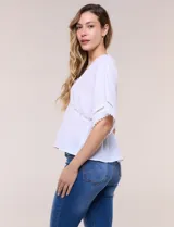 Blusa blanca de poliéster con textura crepada, escote en V con detalles de puntilla, mangas cortas amplias estilo kimono y diseño semi entallado bajo el busto con faldón suelto.