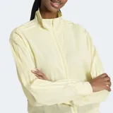 Campera deportiva Adidas Adicolor Sheer, color amarillo pálido, de corte holgado y tejido transparente. Cuenta con cierre frontal, cuello alto, puños y dobladillo acanalados, y las tres tiras características de la marca en las mangas.