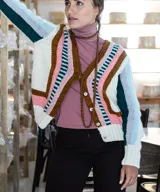 Cardigan tejido a mano en lana merino, con diseño multicolor de bloques geométricos y rayas en tonos blanco, marrón, rosado, celeste y verde. Presenta escote en V, mangas largas y cierre frontal con botones.