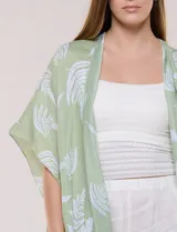Kimono de gasa verde con estampado de hojas blancas y detalles de lurex. Presenta mangas cortas holgadas, diseño abierto al frente y terminación en punta con borlas en el ruedo.