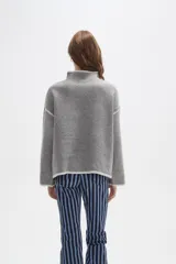 Polera de tejido de punto color negro con detalles de vivos en color beige en el cuello, puños, ruedo y costuras de las mangas. Presenta un diseño holgado con cuello alto y mangas largas.