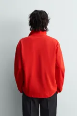 Polo de manga larga color rojo, confeccionado en tejido de algodón con estructura piqué, cuello solapa y cierre frontal de botonadura. Presenta aberturas laterales en el bajo.