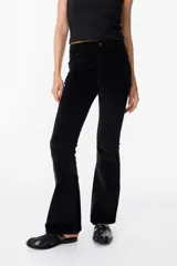 Pantalón de jean tipo pana color negro, de corte acampanado y tiro medio, con cierre frontal y bolsillos laterales.