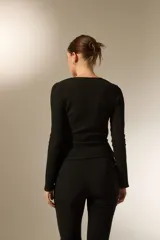 Top de manga larga color negro, con diseño cruzado, escote en V profundo y detalle de argolla lateral. Presenta una textura rugosa y corte asimétrico en el ruedo.