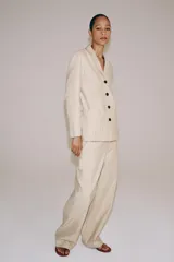 Pantalón barrel de tiro medio confeccionado en hilatura con lino, color beige con diseño a rayas sutiles. Cuenta con cintura con trabillas, bolsillos laterales ocultos en costura, pierna ancha y cierre frontal con cremallera y botón.