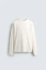 Camiseta de manga larga con corte relajado, confeccionada en tejido de algodón compacto. Presenta cuello redondo y detalle de costura en el centro de la espalda.