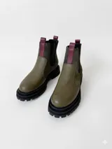 Bota tipo chelsea con plataforma dentada, confeccionada en una combinación de cuero texturizado y gamuza en tonos verde oliva, con detalles de tiradores en color bordó.
