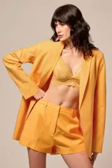 Blazer de corte sastre en color naranja, con solapas clásicas y manga larga. La prenda presenta un acabado texturizado con incrustaciones de strass en toda su superficie, aportando un brillo sutil y sofisticado.