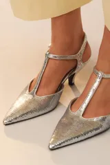Zapato de tacón con cuerpo cubierto de lentejuelas plateadas, diseño con tira en T, cierre de hebilla en el tobillo y acabado en punta.