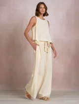 Pantalón palazzo de tiro alto marca Elan, en color beige, confeccionado en mezcla de algodón, viscosa y lino. Presenta cintura delantera plana con parte trasera elastizada, bolsillos laterales funcionales y corte de pierna ancha. Incluye un cinturón trenzado al tono con terminación en borlas y flecos.