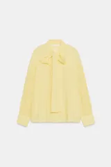 Camisa de rayas finas color amarillo, confeccionada con cuello redondo y lazada en el mismo tejido en el escote. Presenta mangas largas con hombros caídos y puños anchos abotonados.