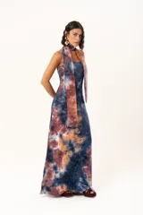 Vestido largo de corte recto y escote strapless, con estampado estilo batik en tonos azul, naranja y bordó. Incluye una bufanda larga integrada al diseño que cae desde el cuello.