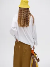 Falda midi de denim color mostaza, con tiro medio, corte recto, cierre frontal de botones metálicos y tajo delantero en el ruedo con terminación deshilachada.