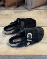 Zuecos negros forrados en corderito sintético, con hebilla metálica decorativa y suela de corcho.