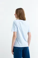 Remera celeste de manga corta y cuello redondo, con estampa frontal en forma de corazón que combina una ola, un atardecer y la frase "Life is Good".