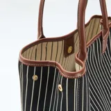 Bolso tipo tote de tela a rayas verticales blancas y negras, con detalles de cuero sintético color suela en la base, manijas y bordes.
