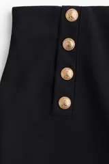 Pantalón negro de punto grueso, tiro alto con elástico oculto, botones dorados decorativos en el frente y piernas rectas de corte holgado.