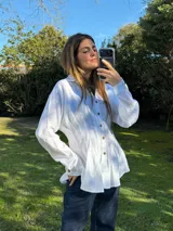 Camisa blanca de silueta entallada con alforzas frontales, cuello clásico, cierre de botones y mangas largas.