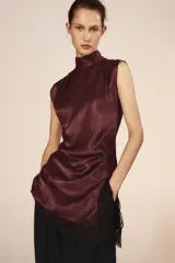 Vestido corto de cuello subido y sin mangas, confeccionado en tejido satinado. Presenta un detalle de fruncido lateral con abertura frontal y aplicación de encaje en el bajo.