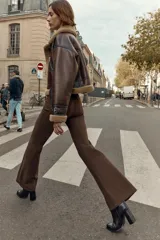 Pantalón de tiro alto color marrón oscuro, con corte flare (campana) y nervio marcado en el frente de ambas piernas. Presenta bolsillos delanteros y bolsillos de plastrón en la espalda.