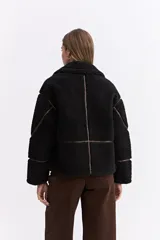 Campera tipo teddy de textura suave y acabado de peluche en color beige. Presenta cuello amplio con detalle de hebilla, cierre frontal y recortes en contraste de color marrón que marcan la estructura de la prenda.