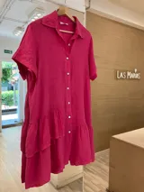 Vestido camisero de lino fucsia, de manga corta, con botones de nácar y un volado en el ruedo final. Además, cuenta con un volado superior en un solo lado, creando un efecto irregular y con diseño.