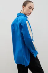 Camisa de corte holgado y largo medio, color negro con detalle de franja lateral en color crema a lo largo de las mangas. Presenta cuello clásico, cierre frontal con botones y tajos laterales en el ruedo.