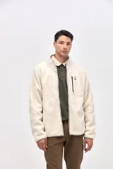 Campera de sherpa con diseño capitoneado en color crema. Presenta cierre frontal completo, cuello alto, bolsillos laterales y un bolsillo en el pecho con cierre en contraste. Incluye detalles en nylon y bordado decorativo en el pecho.