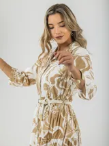 Vestido camisero midi de algodón con estampado floral en tonos rosados y blancos. Tiene cuello camisero, mangas 3/4, botones frontales, falda escalonada y cinturón fino.