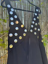 Vestido largo negro con escote en V profundo, tirantes finos y apliques circulares metálicos plateados en el área del busto.