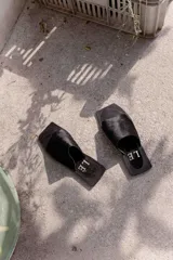 Sandalias planas con punta cuadrada, base negra y capellada de cuero marrón con textura trenzada.