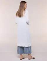 Cardigan largo de punto liviano y suave, de color blanco, con diseño abierto al frente, mangas largas con puños acanalados y bolsillos frontales aplicados.