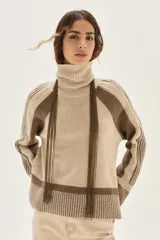 Polera de cuello alto confeccionada en lana lambswool, con diseño de bloques de color en tonos beige y marrón. Presenta mangas raglán con textura acanalada y detalles en hilo metalizado lurex.