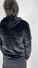 Canguro de peluche negro con cierre parcial frontal, capucha y bolsillo tipo canguro.