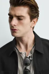 Sobrecamisa negra de corte relajado, confeccionada en tejido con mezcla de algodón elástico. Presenta cuello solapa, cierre frontal de cremallera, bolsillos de plastrón en el pecho y bolsillos de vivo en la cadera.