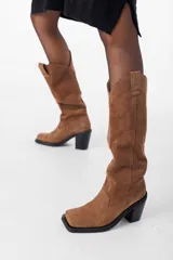 Bota de caña alta color beige, de cuero gamuzado, con taco cuadrado y punta cuadrada.