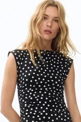 Vestido midi entallado de punto elástico en color negro con estampado de lunares blancos. Presenta escote bote, mangas japonesas y laterales fruncidos que realzan la silueta.