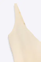 Body color beige claro, de tejido liso, con escote en pico pronunciado y tirantes anchos ajustables. Presenta cierre inferior con botones a presión.