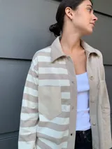 Camisa color beige con rayas horizontales blancas, de corte recto, cuello camisero y cierre frontal con botones.