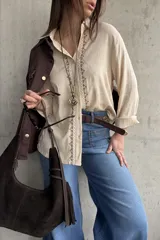 Camisa beige de tejido liviano y calce relajado, con manga larga y detalle de puntilla y bordado en contraste que recorre el frente.