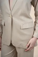 Blazer de lino y viscosa color beige, de calce relajado, con solapa clásica, cierre de un botón frontal y bolsillos con solapa en la parte delantera.