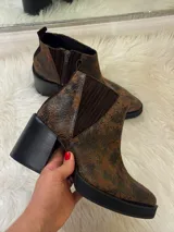 Bota corta tipo botineta de cuero con acabado texturizado efecto gastado en color chocolate. Presenta paneles laterales de elástico acanalado al tono, cierre lateral interno, plataforma delantera y taco cuadrado robusto en color negro.