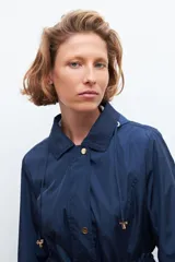 Campera impermeable azul marino con capucha desmontable, cierre frontal con botones a presión y cordón ajustable en la cintura.